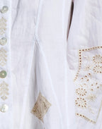 Close-up of a white garment with intricate gold embroidery and button details.