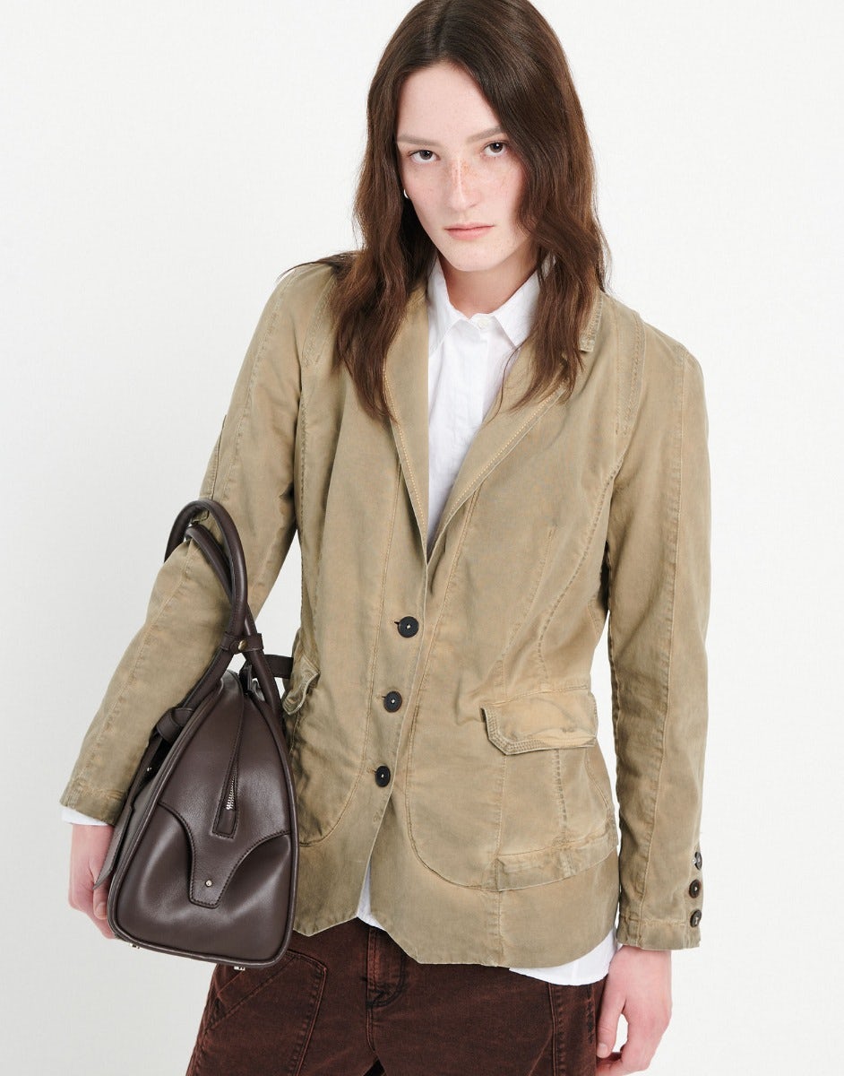 Woman wearing a beige blazer holding a brown leather bag on a white background