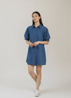 Woman wearing a blue denim dress against a plain background. Antonia play denim dress