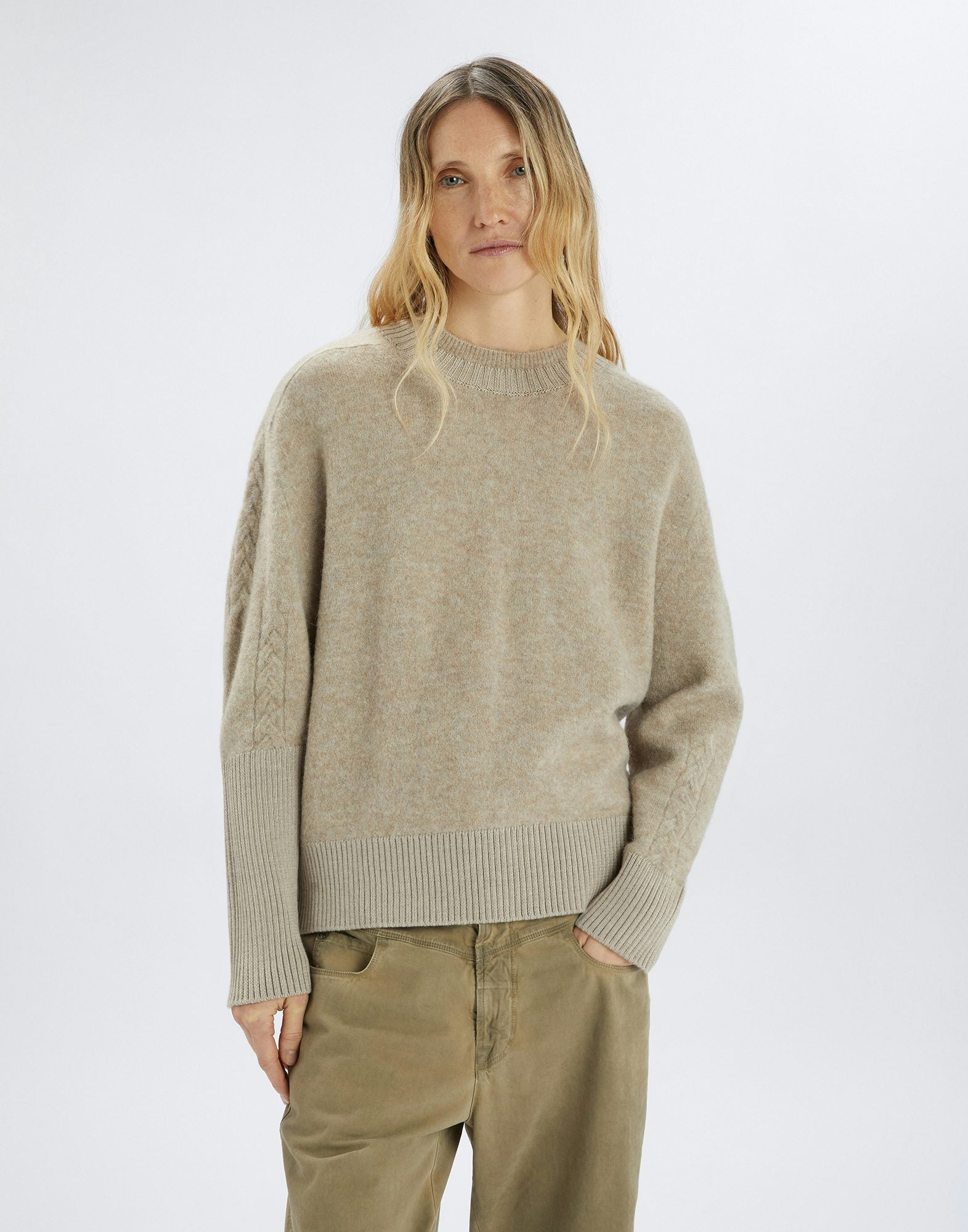 Woman wearing a beige sweater and pants on a white background