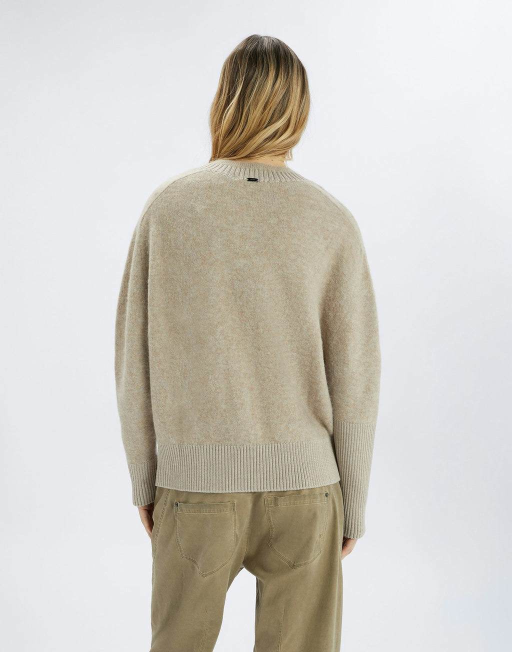 Person wearing a beige sweater and pants on a white background