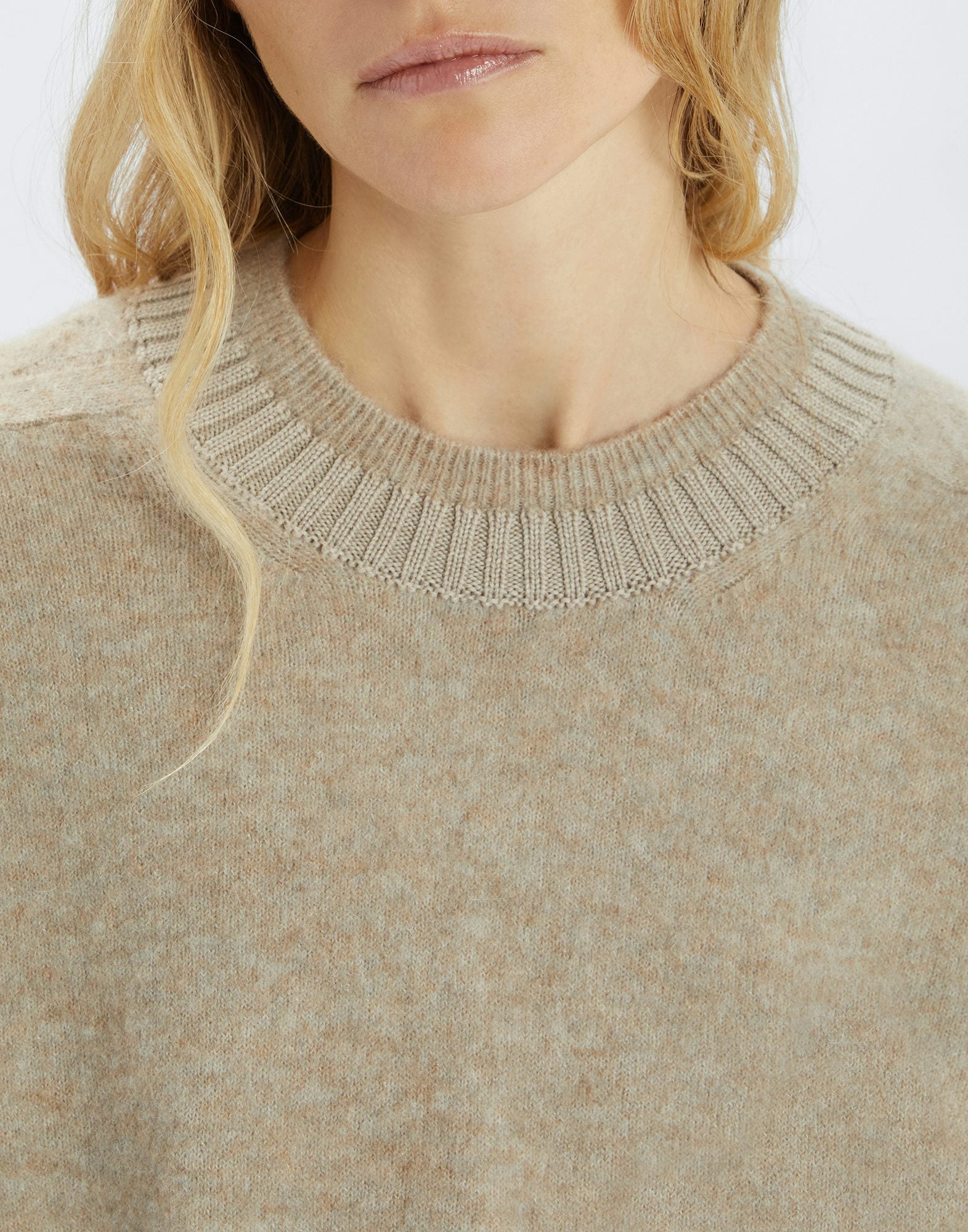 Close-up of a beige sweater with a ribbed neckline on a white background