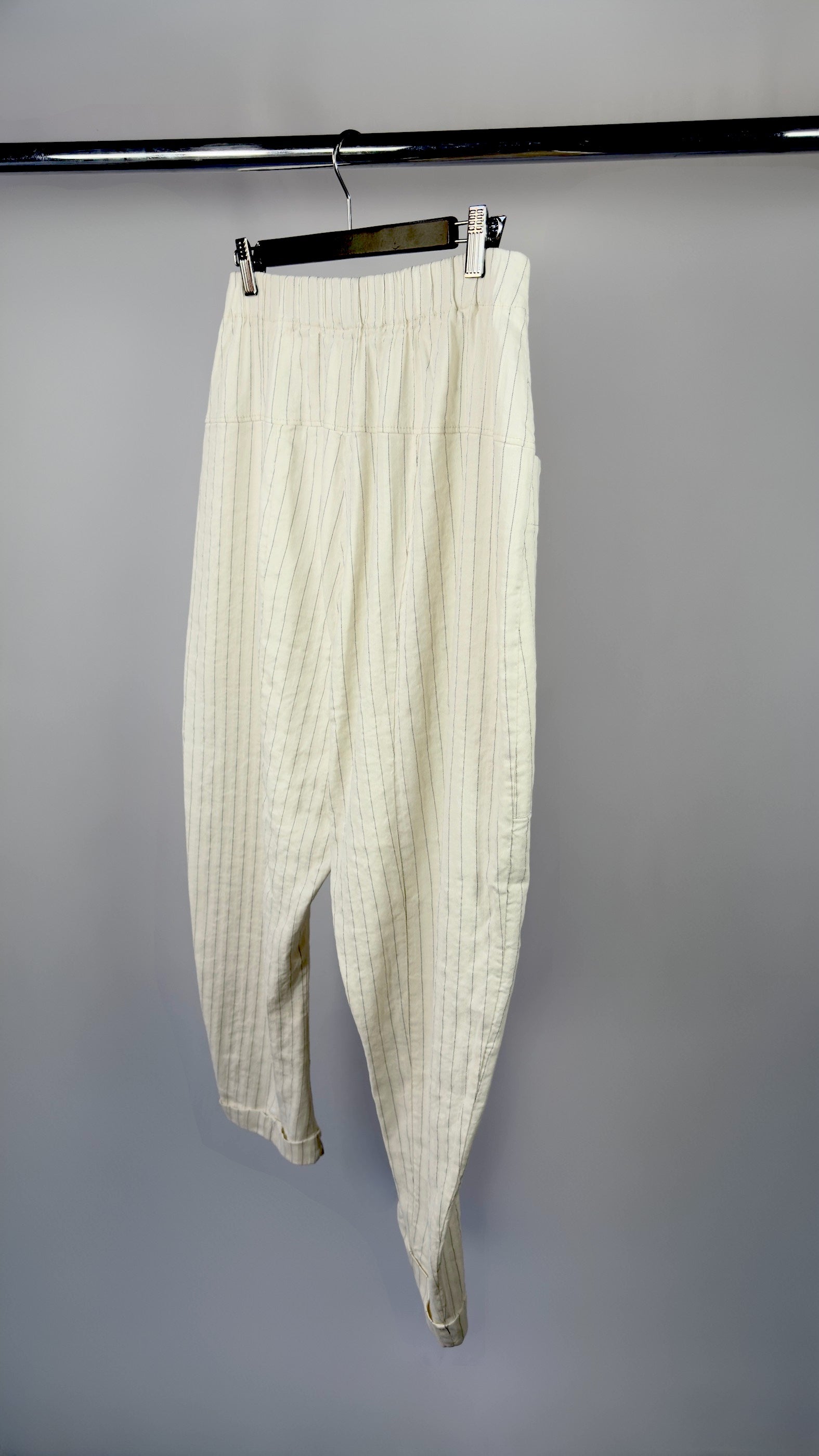 White pleated pants hanging on a black rack against a gray background