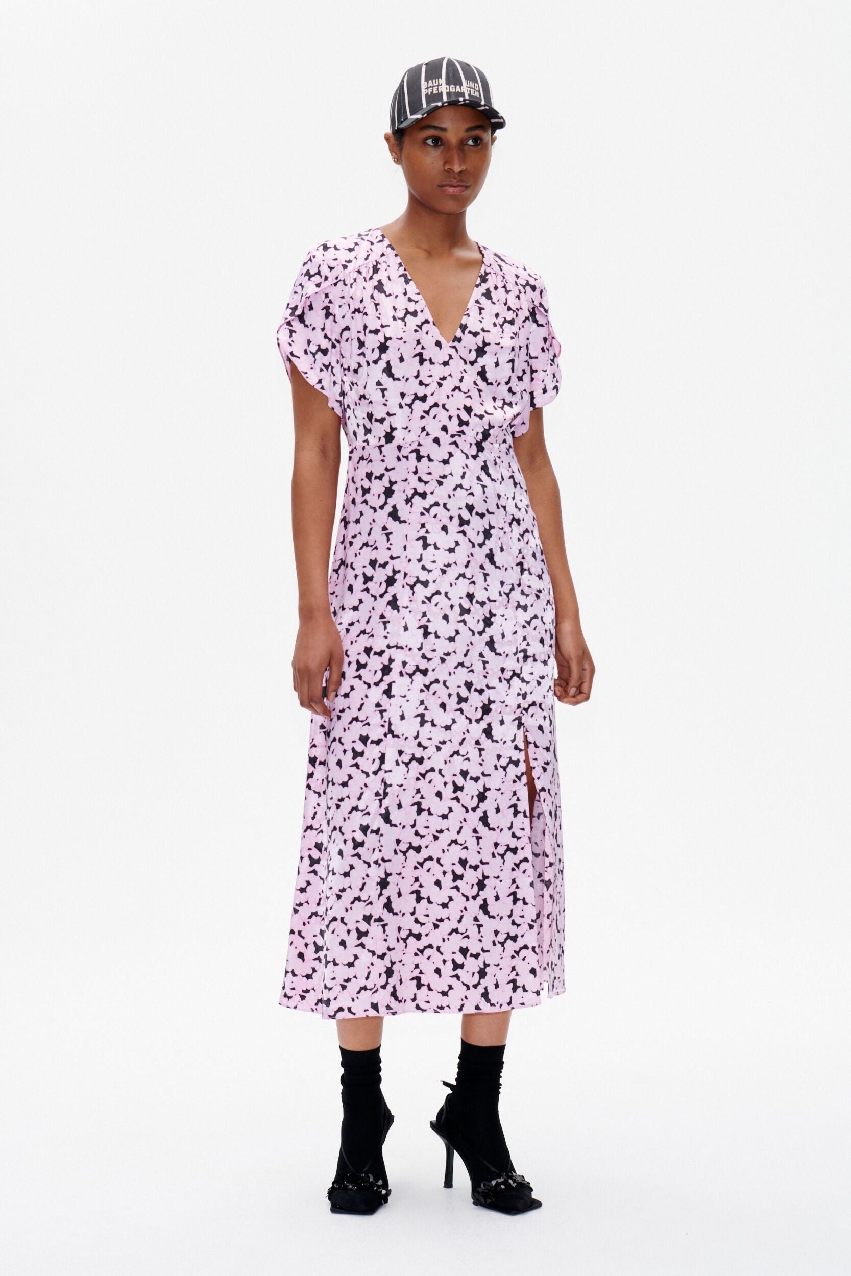 A person standing wearing a mid-calf length pink floral dress with cap sleeves and a V-neck neckline.