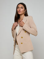 Woman wearing a beige blazer with gold buttons on a plain background