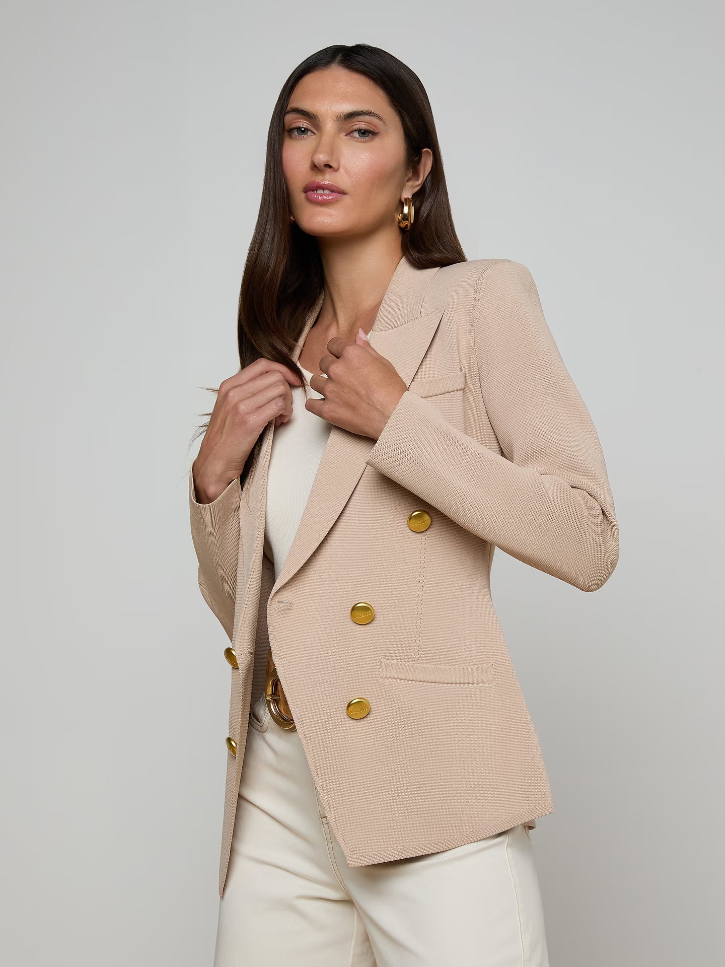 Woman wearing a beige blazer with gold buttons on a plain background