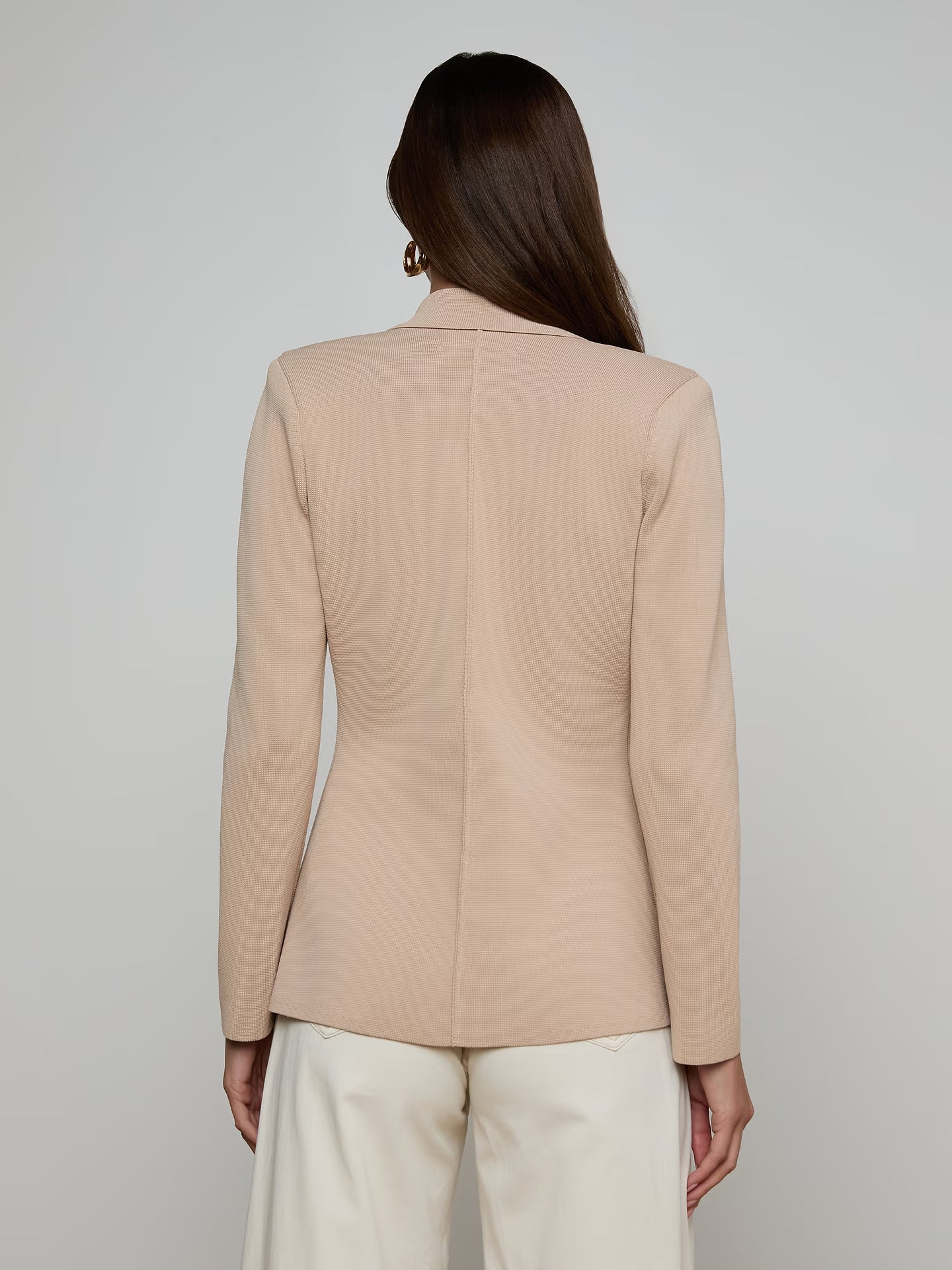 Person wearing a beige blazer against a plain background