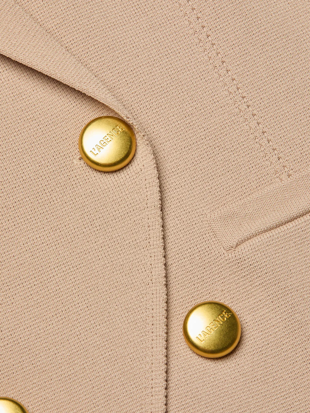 Close-up of beige fabric with gold buttons featuring a brand logo.
