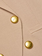 Close-up of beige fabric with gold buttons featuring a brand logo.