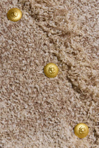 Close-up of a beige textured faux fur or shag carpet with three round gold decorative buttons arranged diagonally.