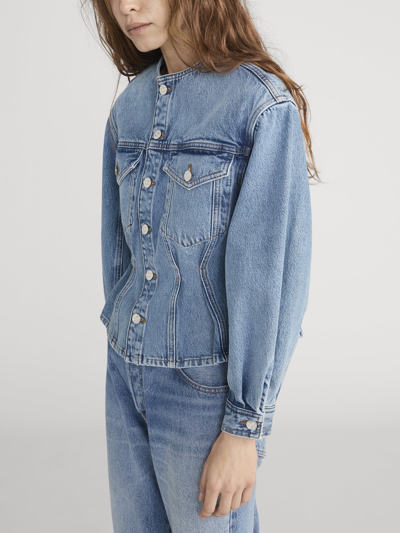 Person wearing a blue denim jacket and jeans on a plain background