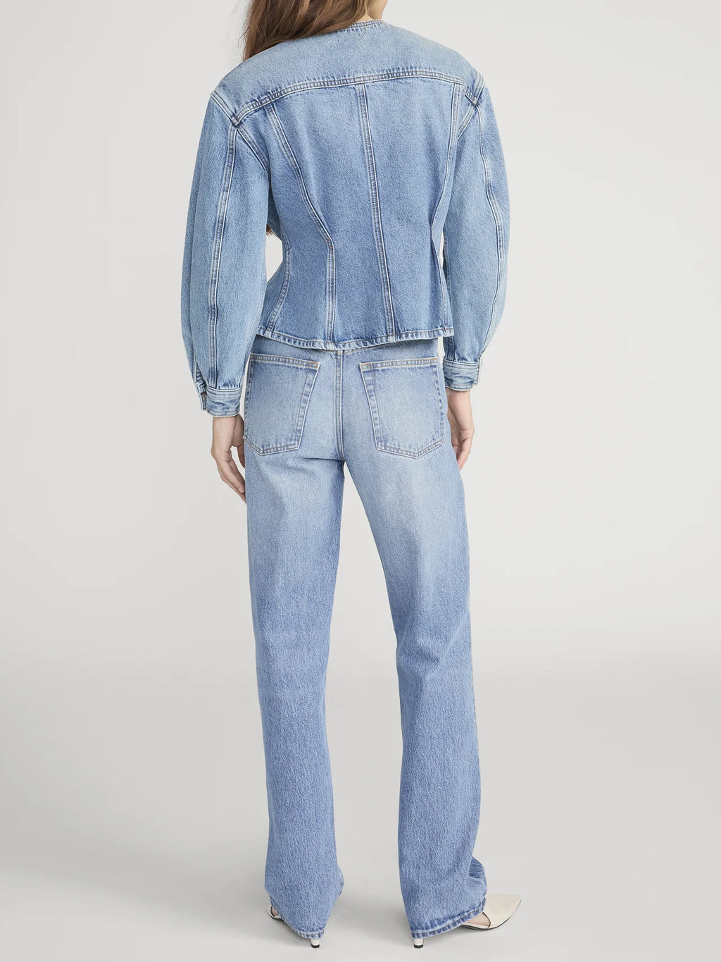 Person wearing a light blue denim jacket and jeans on a white background