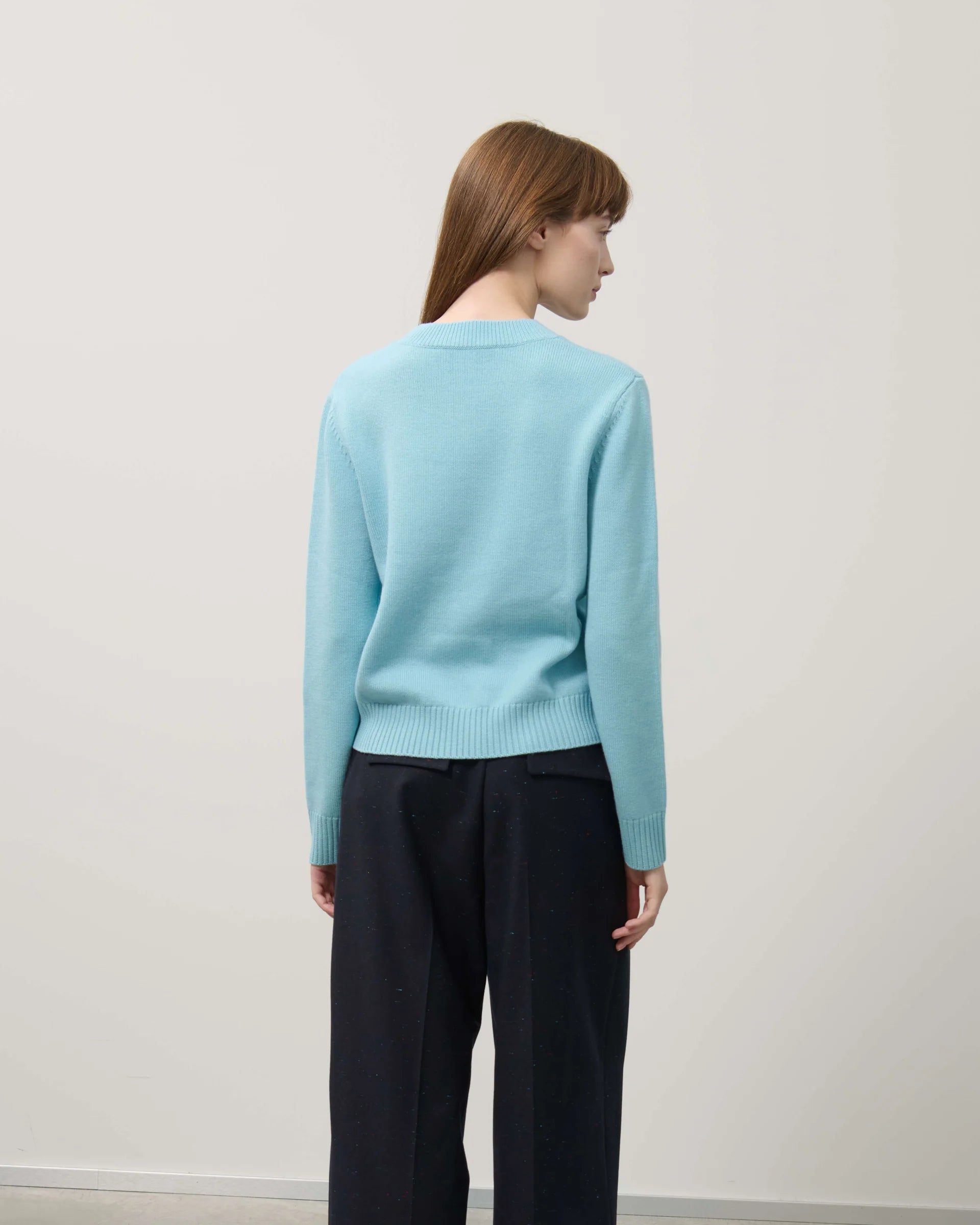 Person wearing a light blue sweater and dark pants against a white background