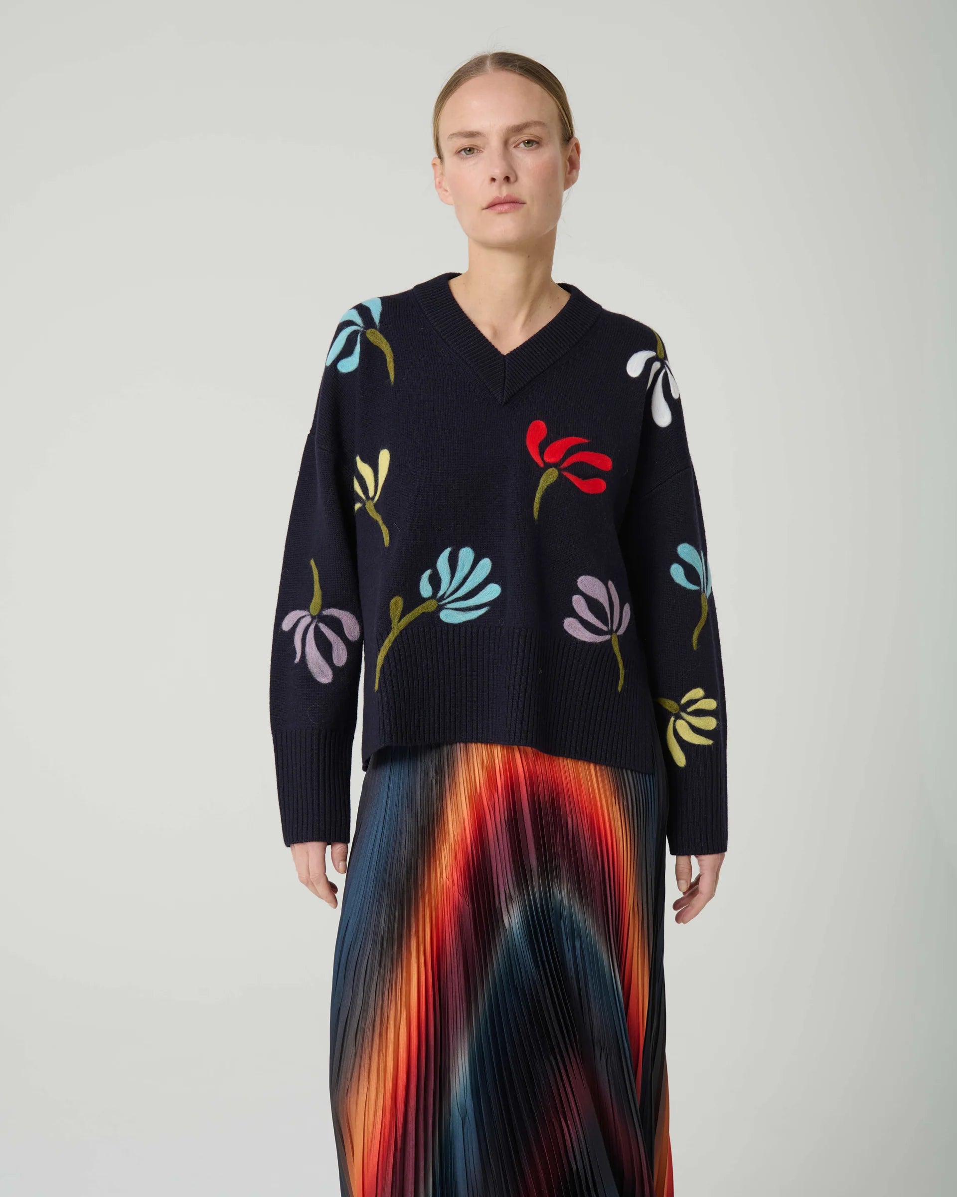Woman wearing a navy sweater with colorful floral patterns on a plain background