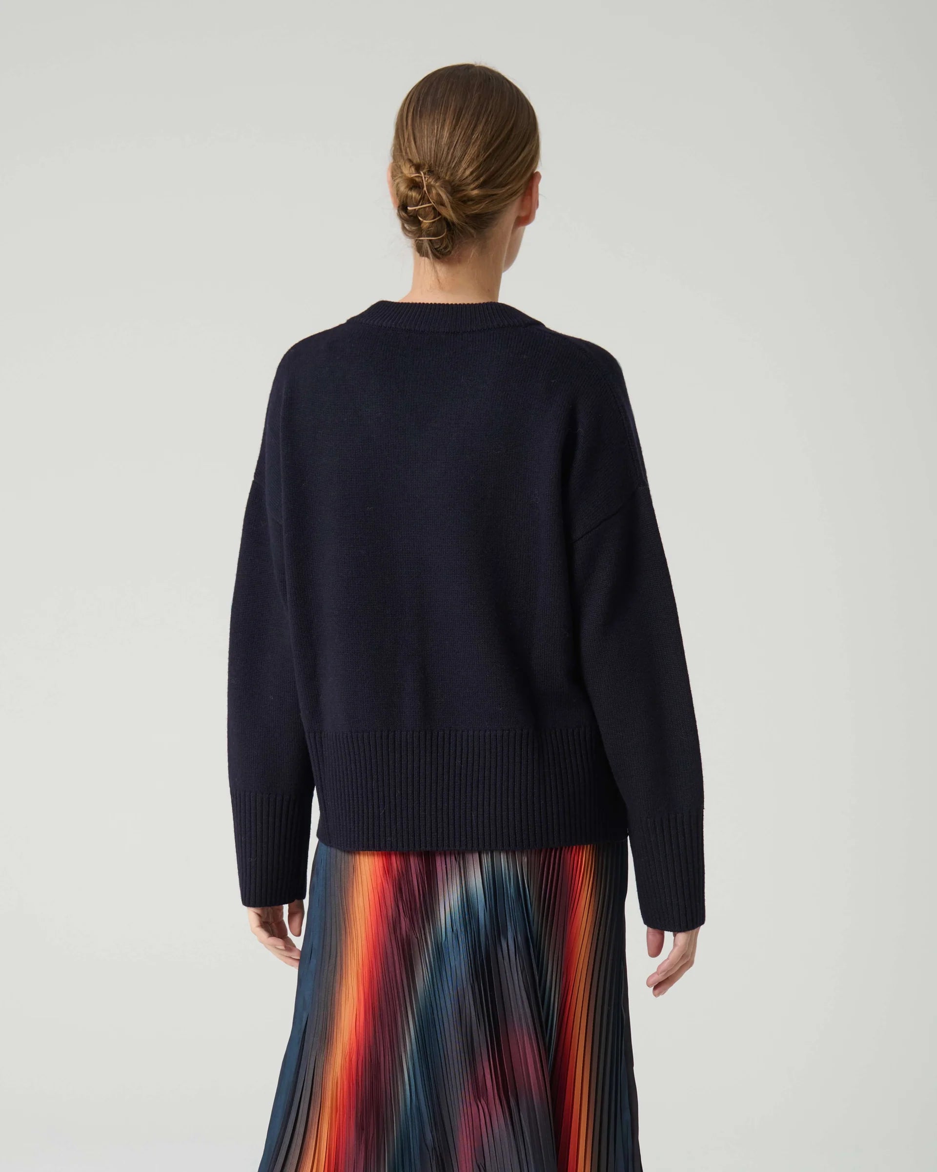 Person wearing a dark blue sweater with a colorful skirt on a light gray background