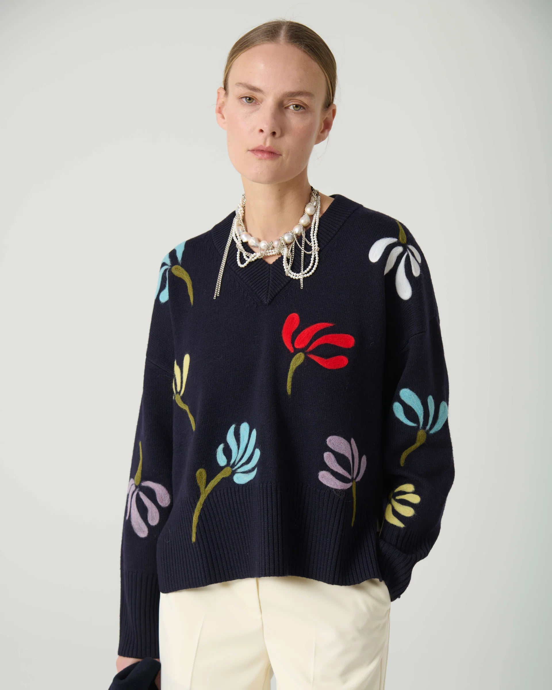 Person wearing a navy sweater with colorful floral patterns on a plain background