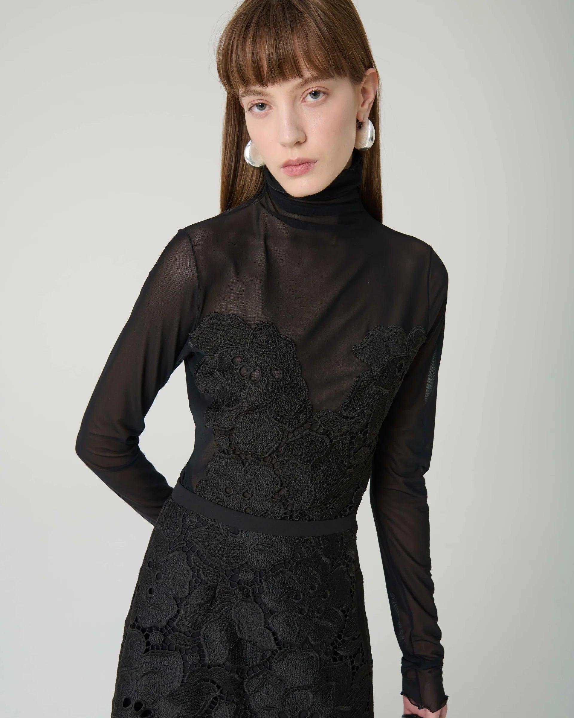 Woman wearing a black lace dress against a plain background