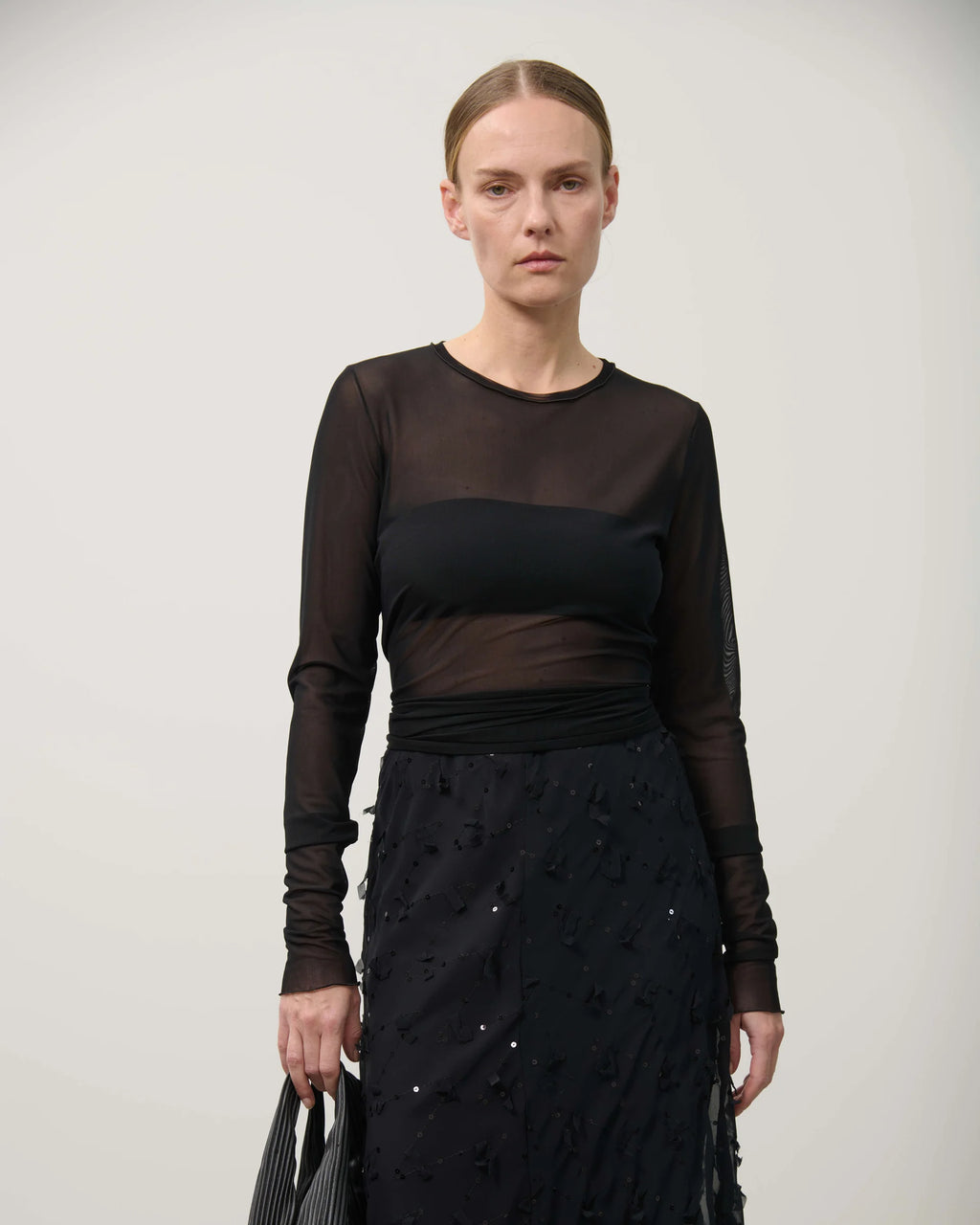 Woman wearing a black outfit with sheer sleeves against a plain background