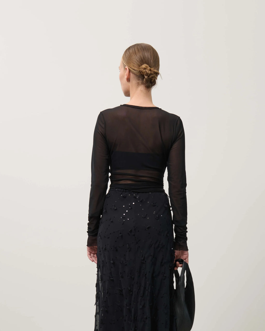 Person wearing a black long-sleeve top and black skirt with sequins on a white background