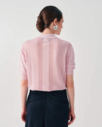 A woman shown from the back wearing a light pink short-sleeve knit top with a vertical textured stripe down the center back, paired with dark navy pants, against a plain light gray studio background.