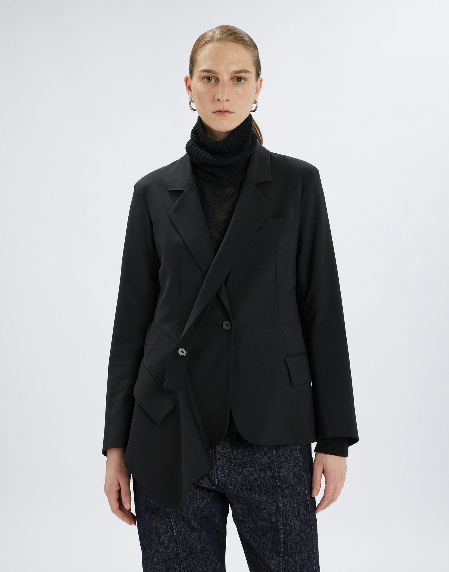 Person wearing a black blazer over a black turtleneck on a white background