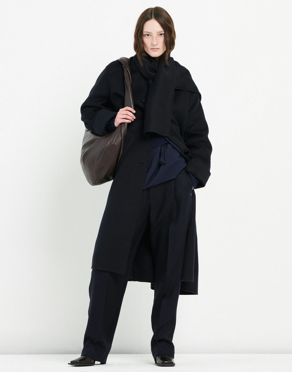 Person wearing a black coat and pants holding a brown bag on a white background