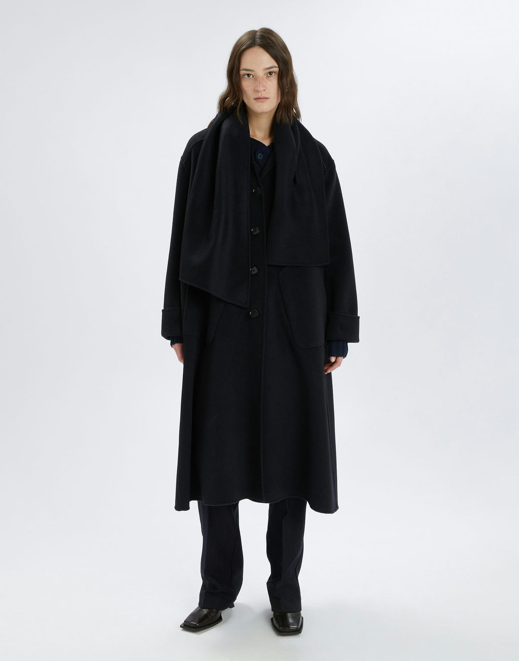 Person wearing a long black coat and pants on a white background