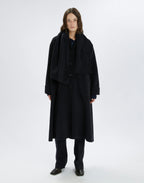 Person wearing a long black coat and pants on a white background