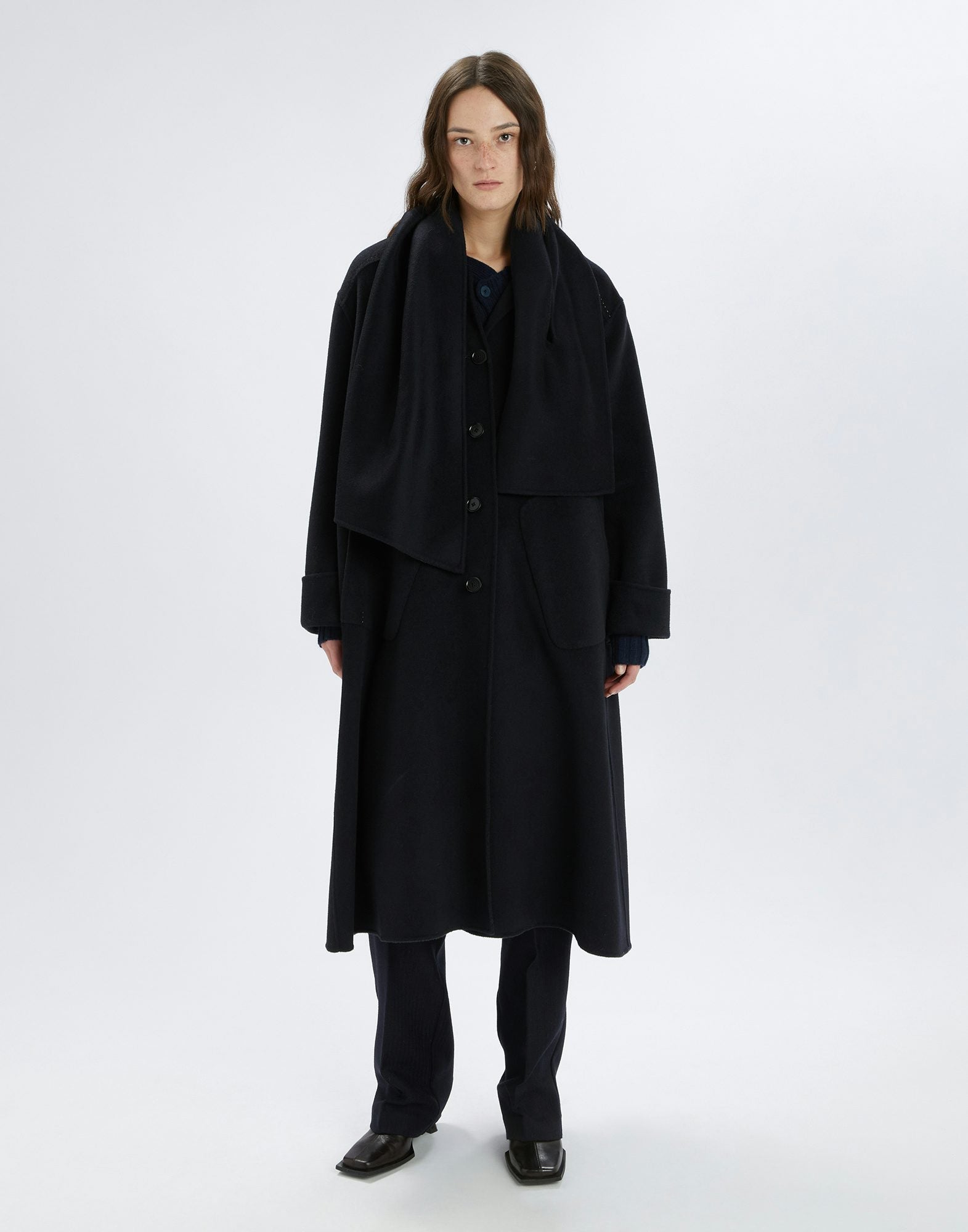 Person wearing a long black coat and pants on a white background