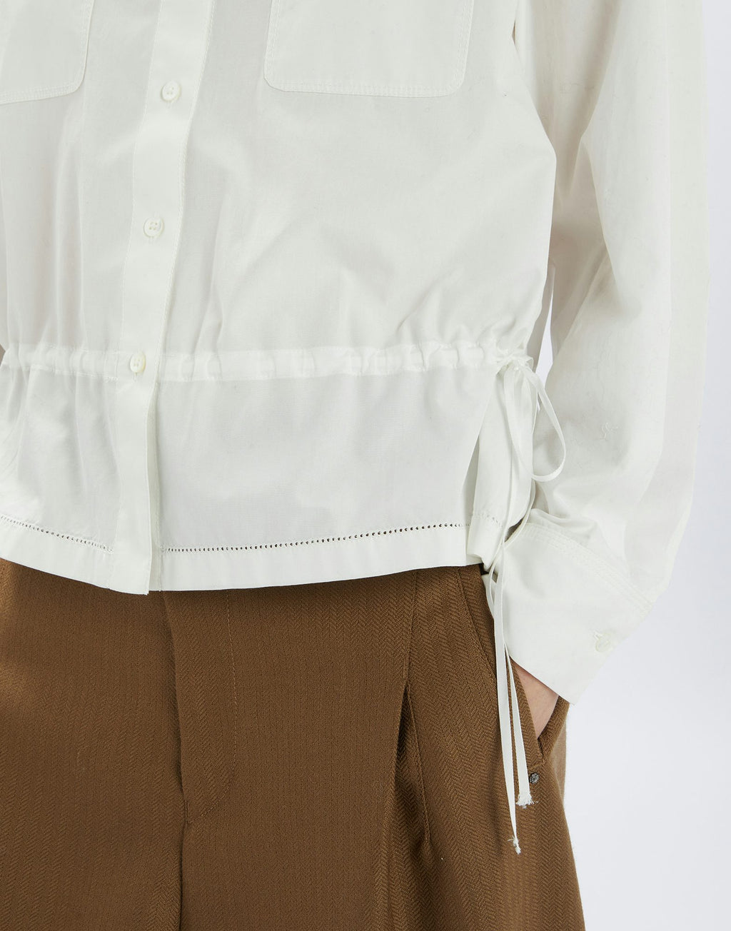 White shirt with a tie detail worn with brown pants on a white background