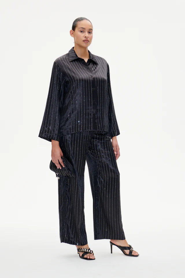 A model wearing black wide-leg trousers with an elasticated waistband and crystal detailing, from the BAUM UND PFERDGARTEN Pre-Spring 2024 collection.