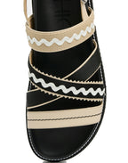 Black sandal with beige and white striped straps on a white background