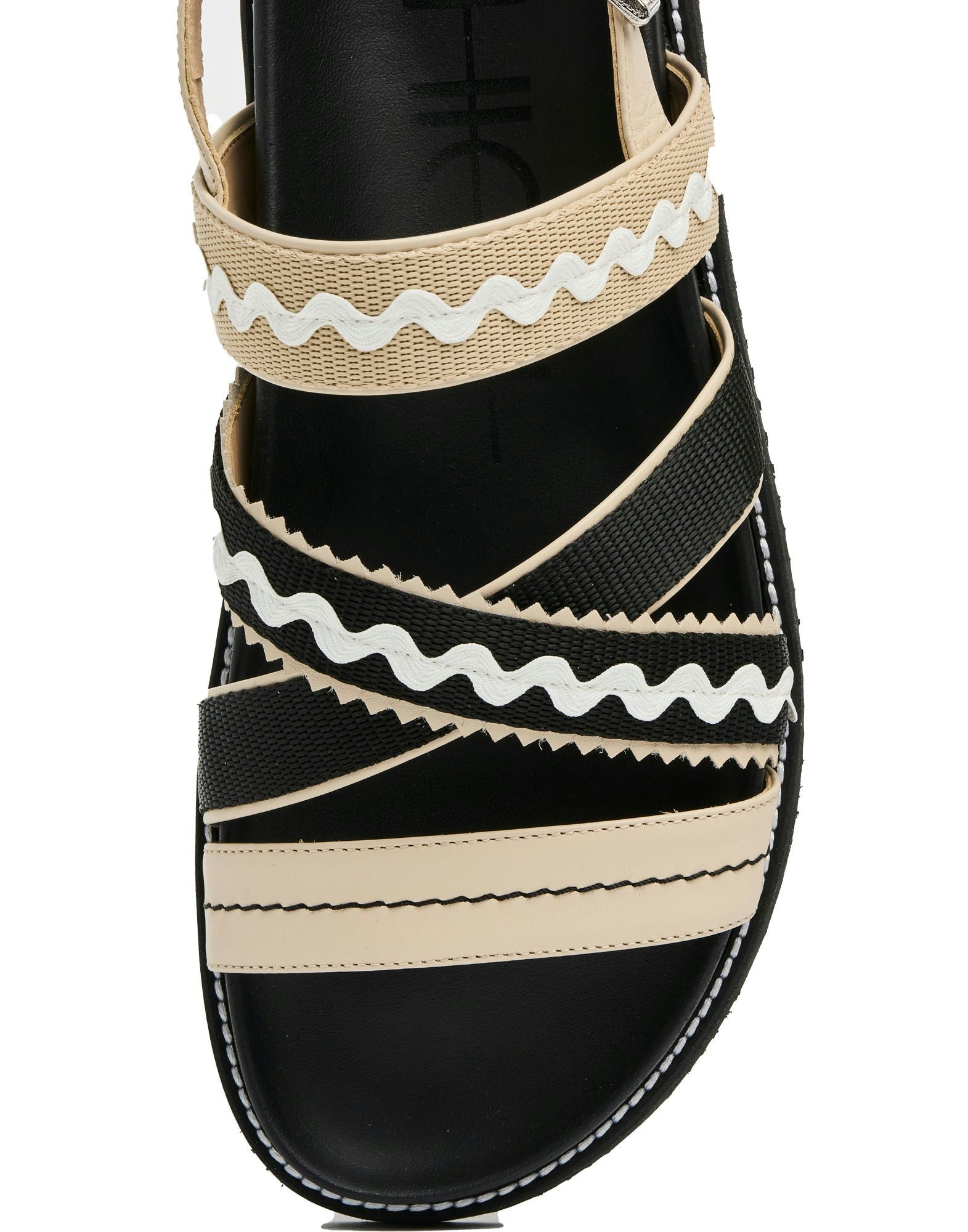 Black sandal with beige and white striped straps on a white background
