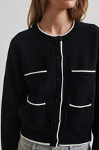 Black cardigan with white trim worn by a person on a plain background