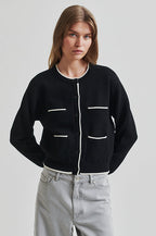 Person wearing a black cardigan with white accents on a light gray background