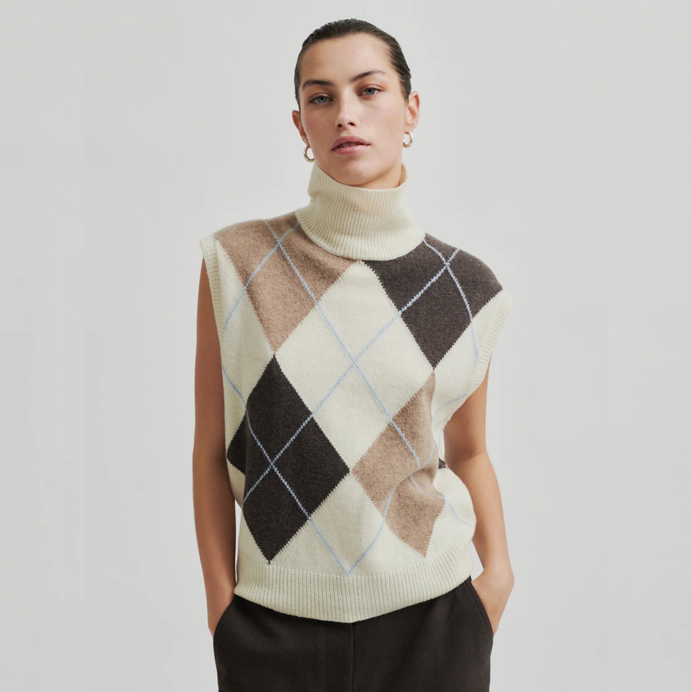 A woman wearing a beige, brown, and white checkered sleeveless high-neck vest.
