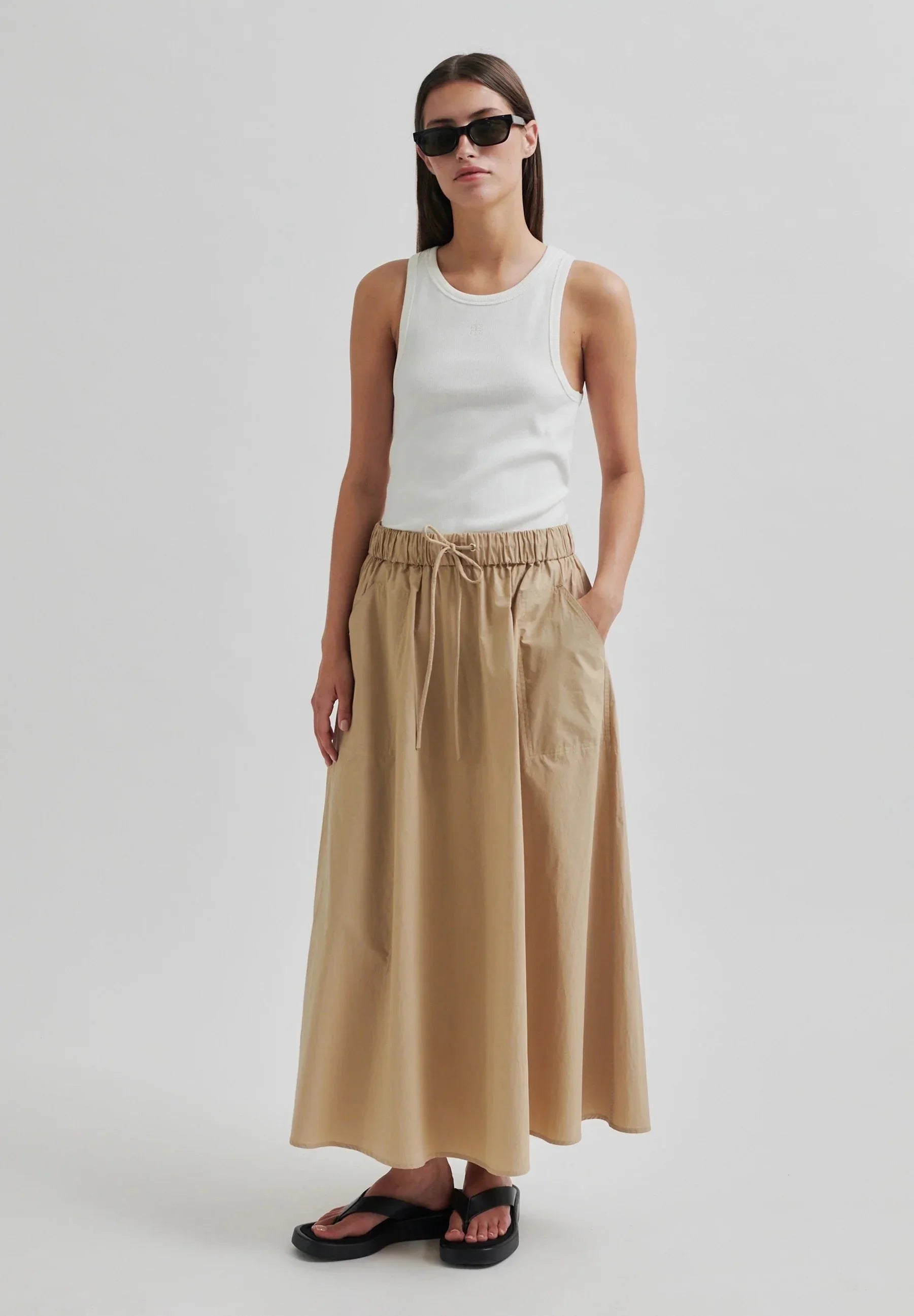 Woman wearing a white sleeveless top and beige wide-leg pants on a plain background