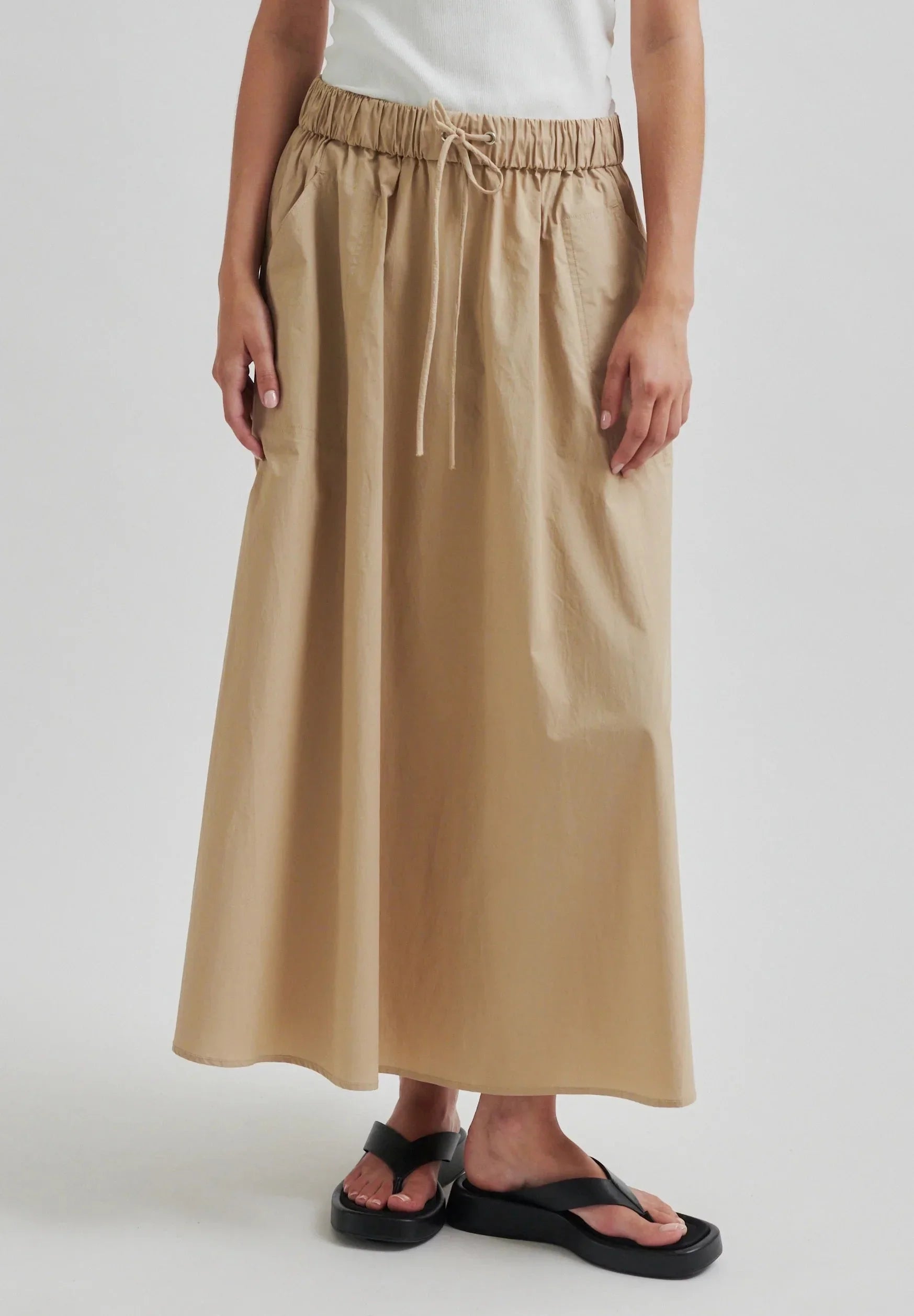 Person wearing a beige skirt with an elastic waistband on a white background