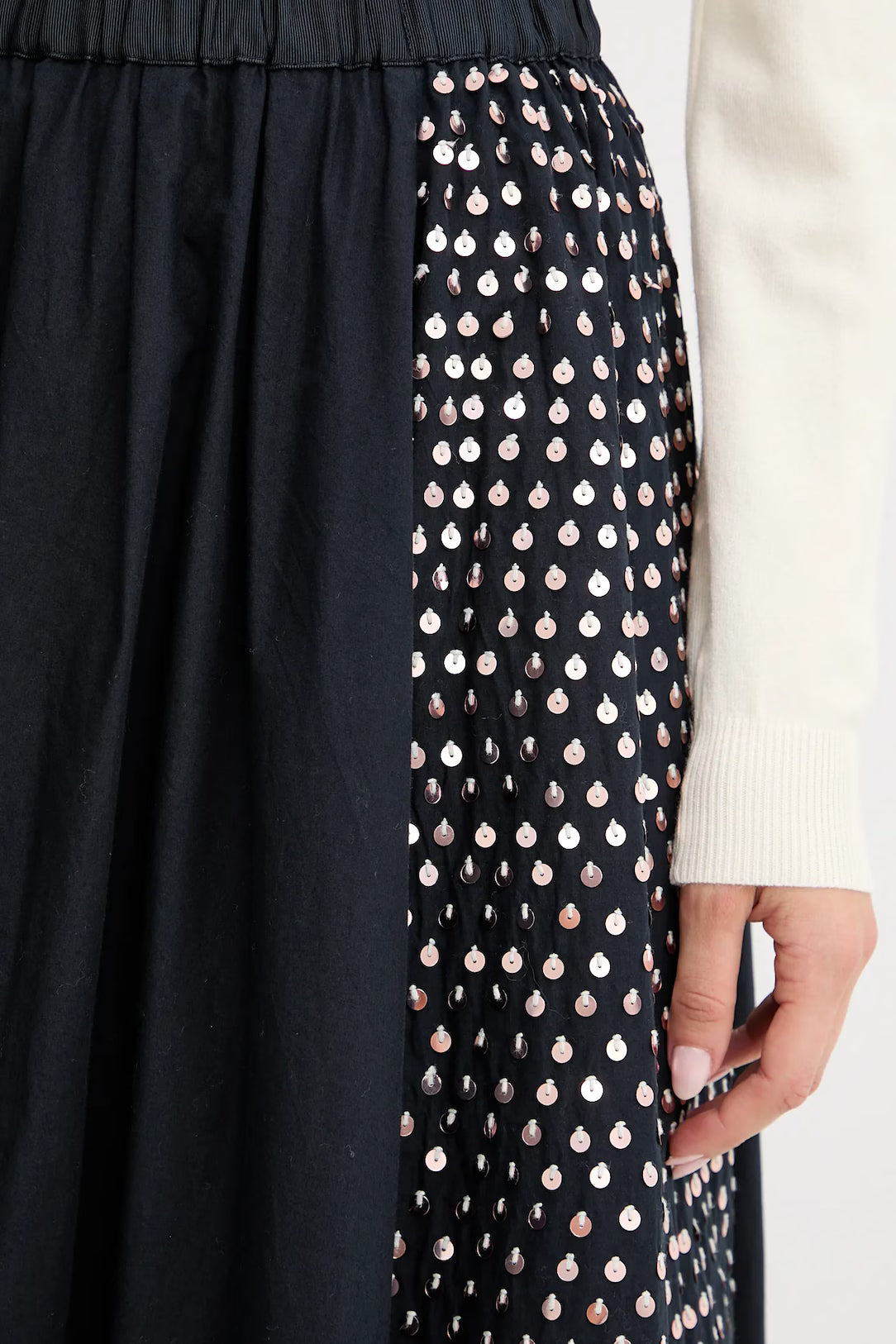 Black skirt with a patterned hem and white sweater sleeve.