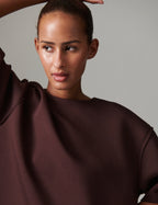 Woman wearing a dark brown garment against a neutral background