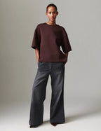 Person wearing a brown oversized shirt and dark gray pants on a plain background