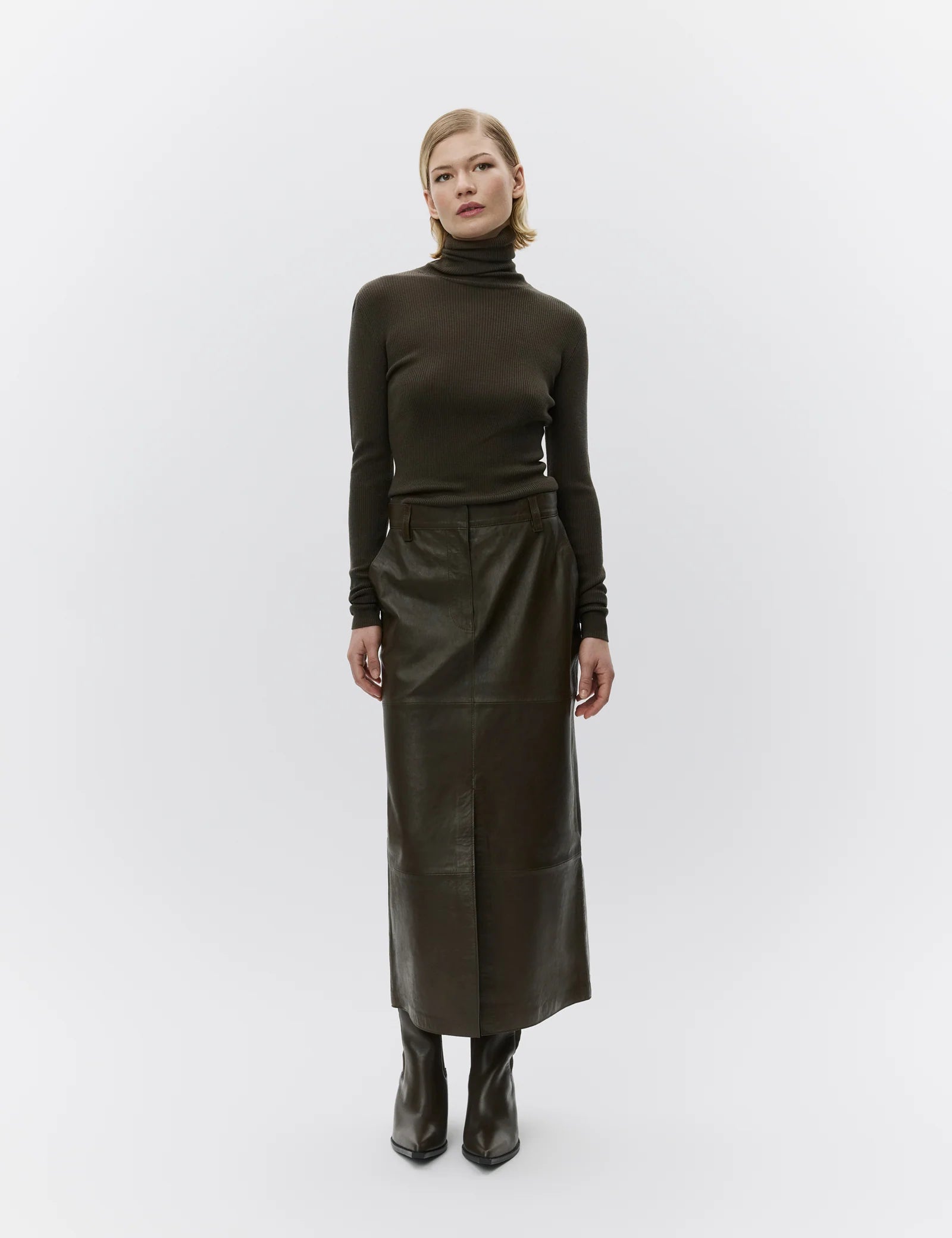 Woman wearing a dark green turtleneck and leather skirt on a white background
