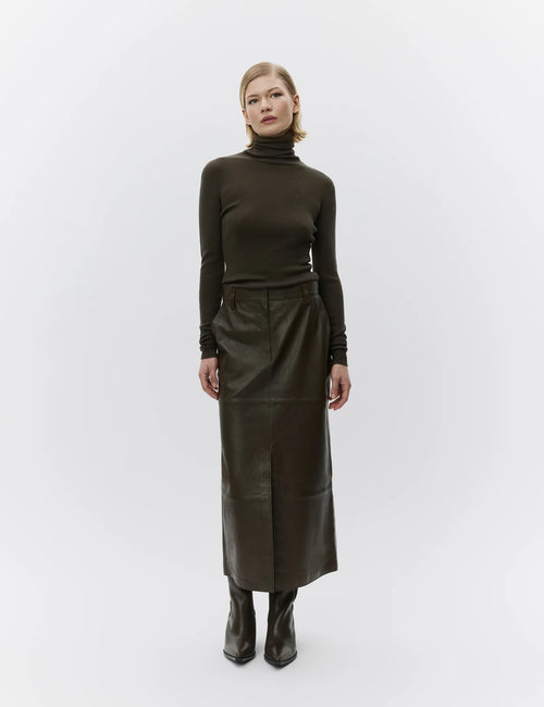 Woman wearing a dark green turtleneck and leather skirt on a white background