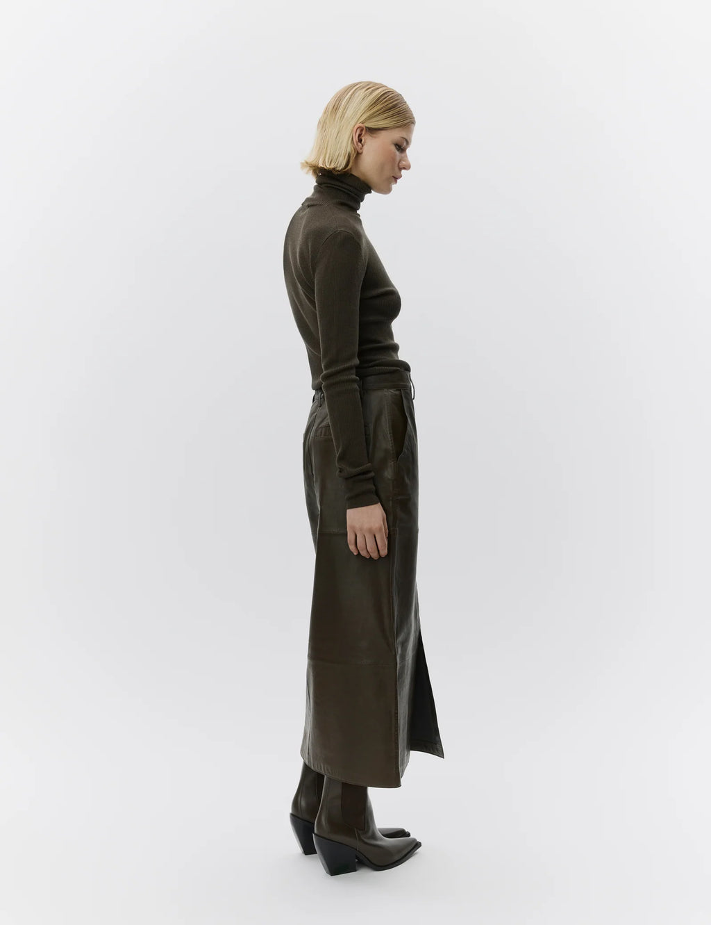 Woman wearing a long dark green leather skirt and turtleneck on a white background