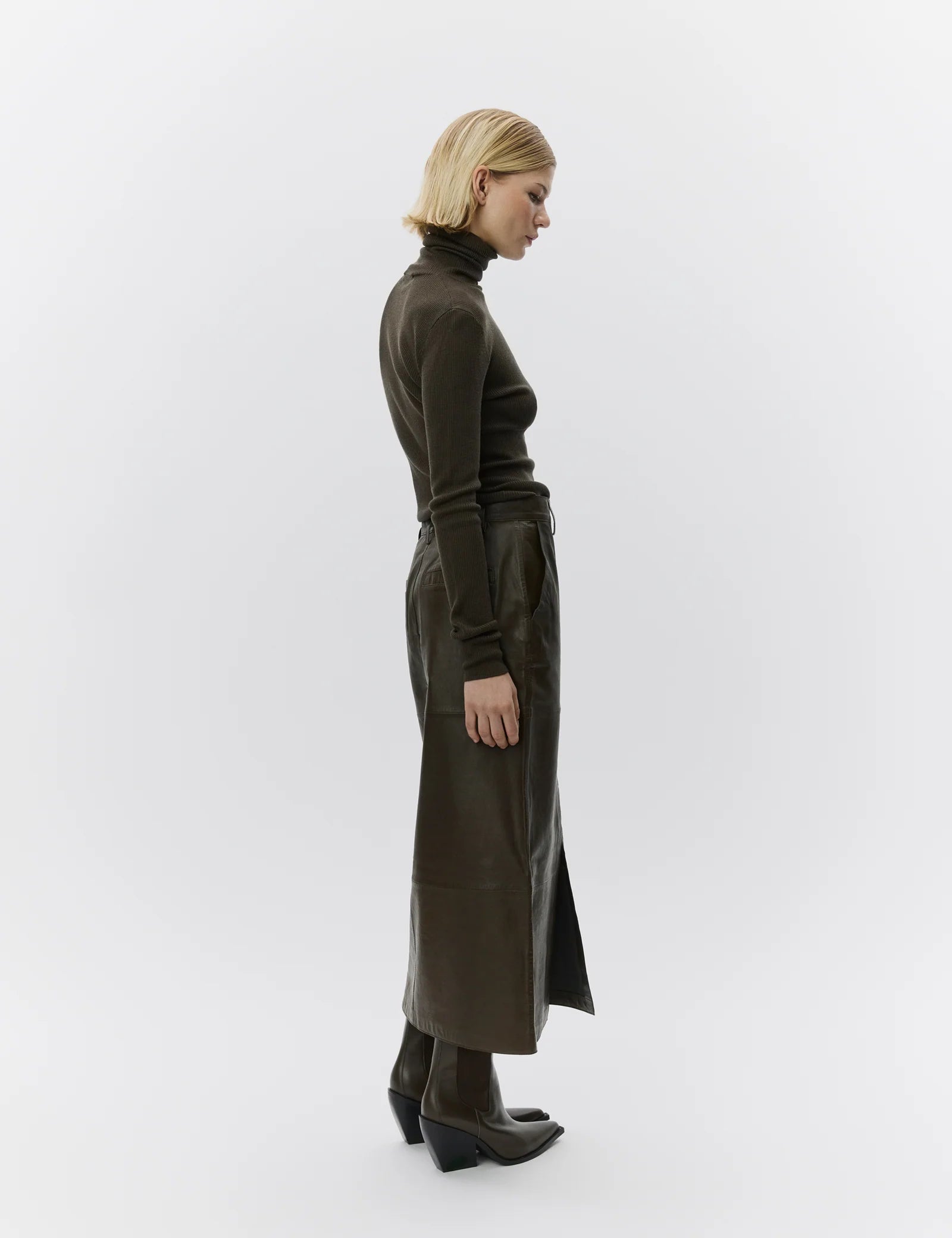Woman wearing a long dark green leather skirt and turtleneck on a white background