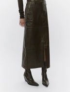 Person wearing a long dark brown leather skirt and black boots on a white background