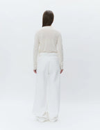 Person wearing a beige sweater and white pants on a white background