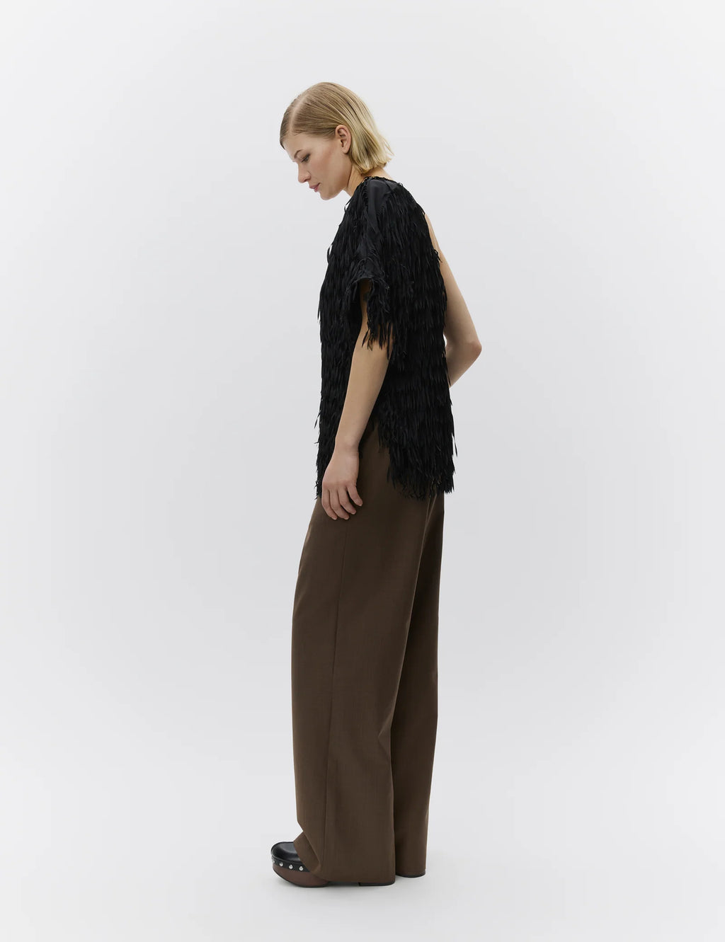 Woman wearing a black fringed top and brown pants on a white background