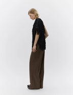 Woman wearing a black fringed top and brown pants on a white background