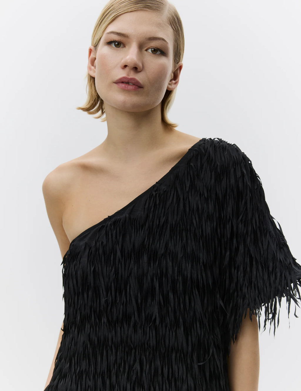 Woman wearing a black one-shoulder dress with fringe details on a white background